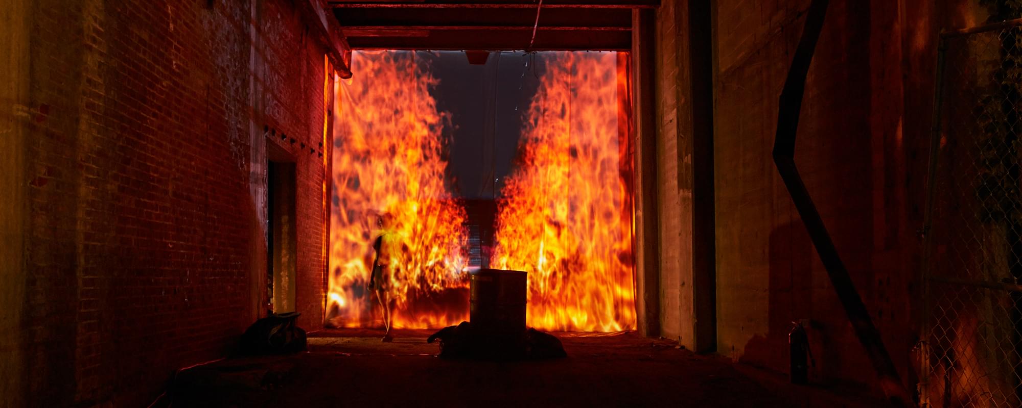 Night time photograph of a tunnel onto which is projected a faux 3D perspective of a firescape stretching backwards in a narrow column into infinity