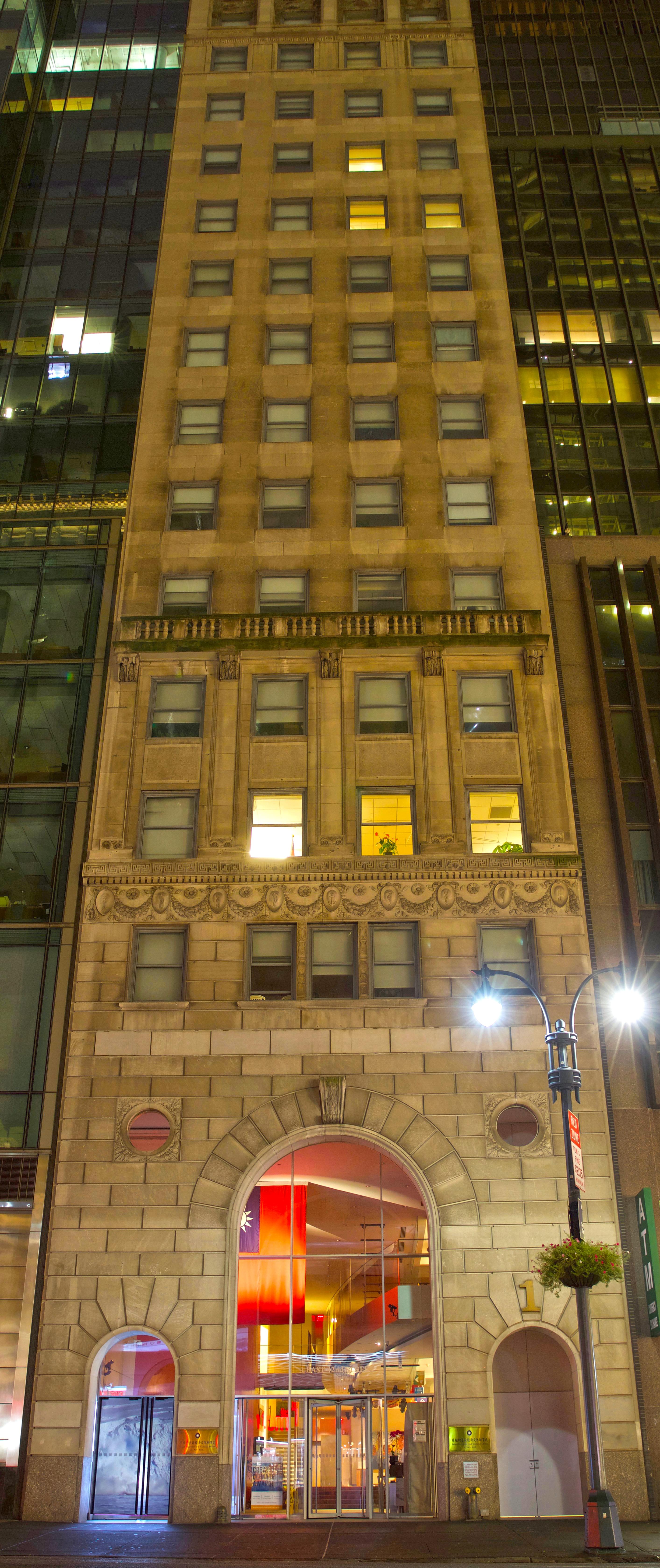 Extremely tall vertical photograph that encompasses approximately 15 stories of the facade of a beige apartment building. On street level, projected into the windows of the building's entrance, is an Arctic landscape with a large glacier in the middle of the frame.