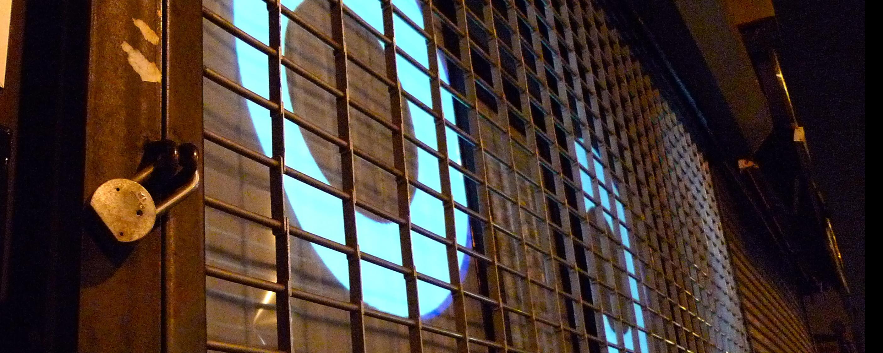 Nighttime, close-up photograph of two large, cartoonish eyes projected into a storefront window behind a metal security gate