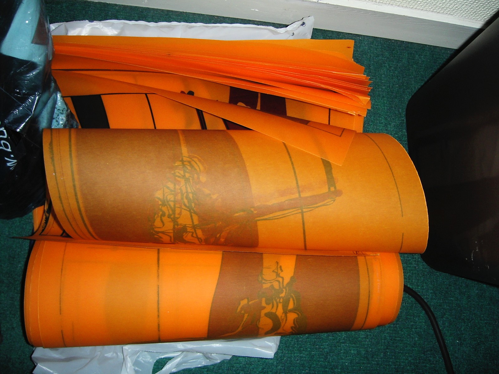 Photograph of rolled-up screen prints, on golden yellow/orange paper sitting on the floor.